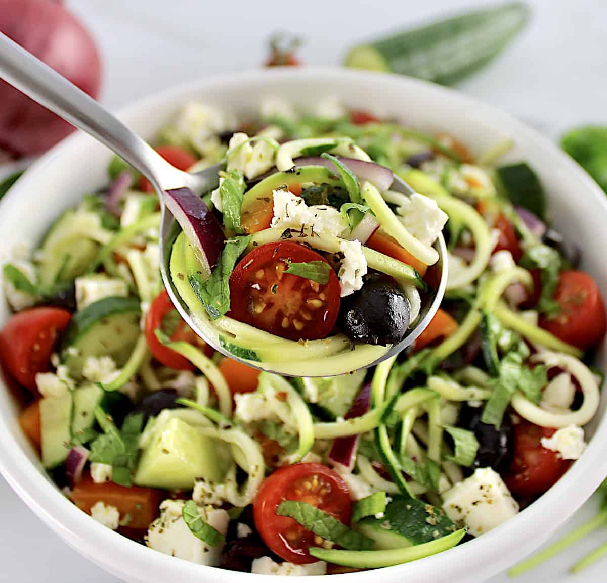 Greek Zucchini Pasta Salad in spoon held up over salad in white bowl