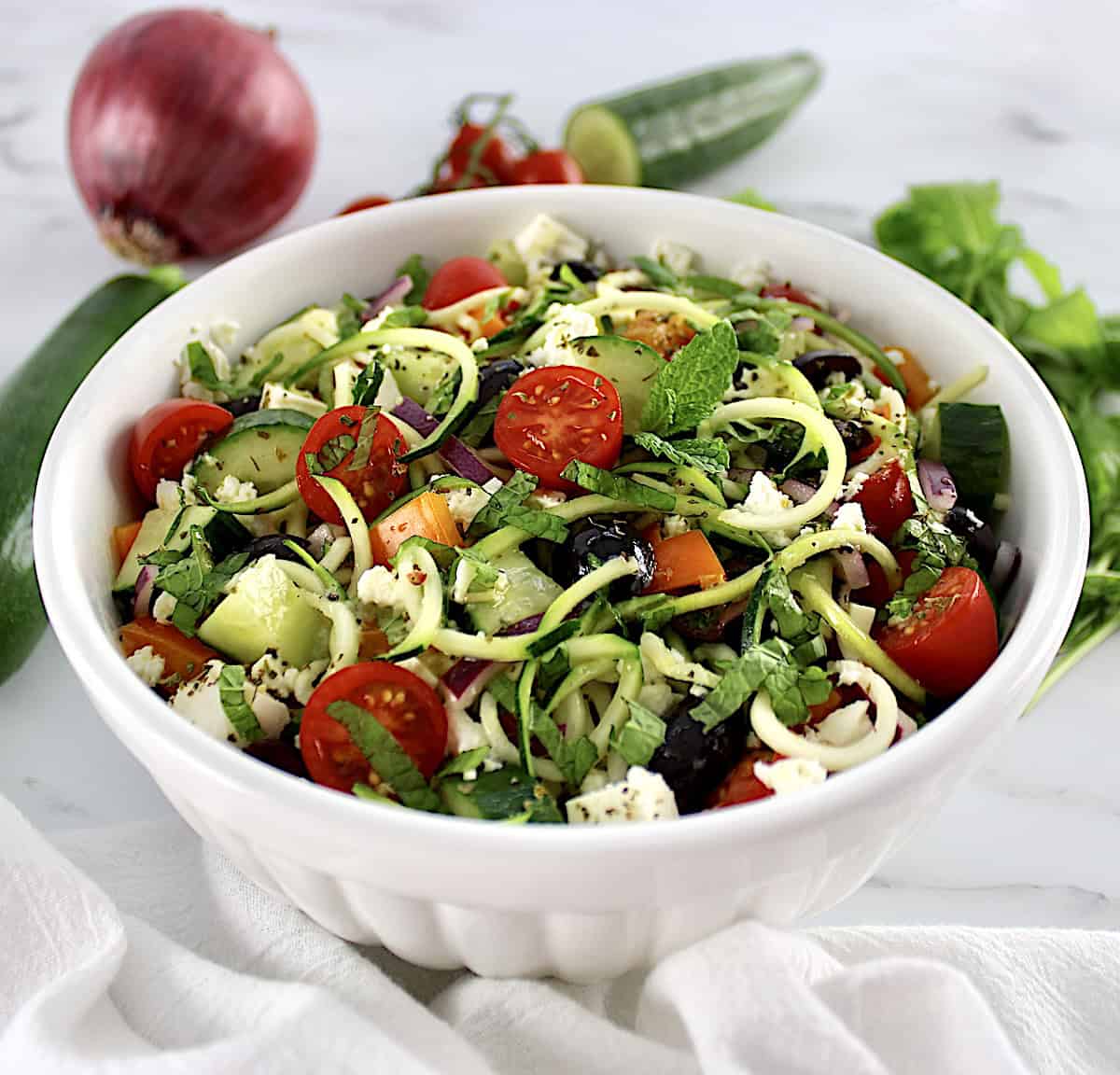 Greek Zucchini Pasta Salad in white bowl with veggies in back