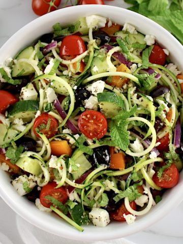 overhead view of Greek Zucchini Pasta Salad in white bowl with veggies in back