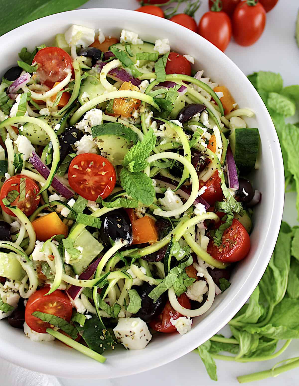 overhead view of Greek Zucchini Pasta Salad in white bowl with veggies in back