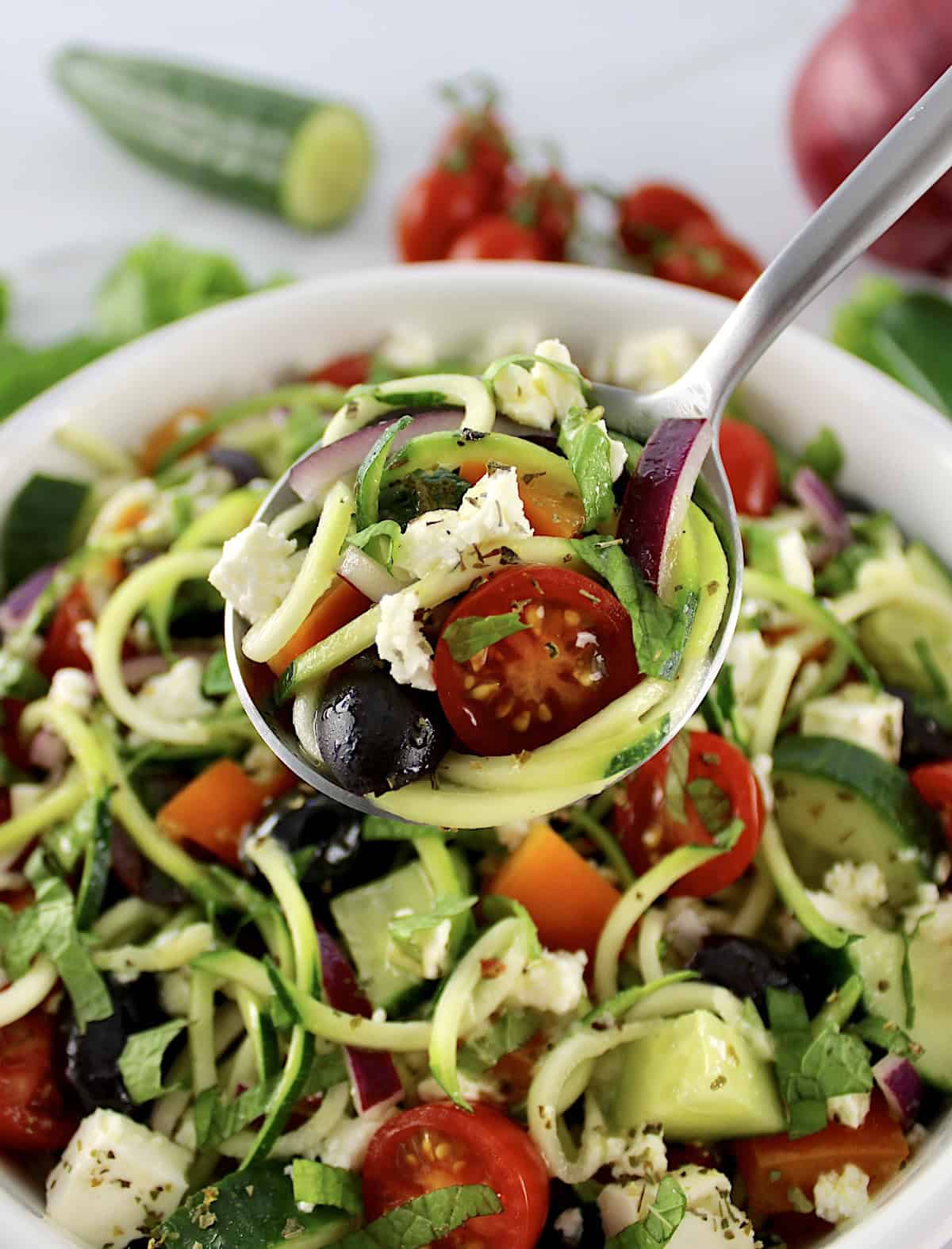 Greek Zucchini Pasta Salad in spoon held up over salad in white bowl