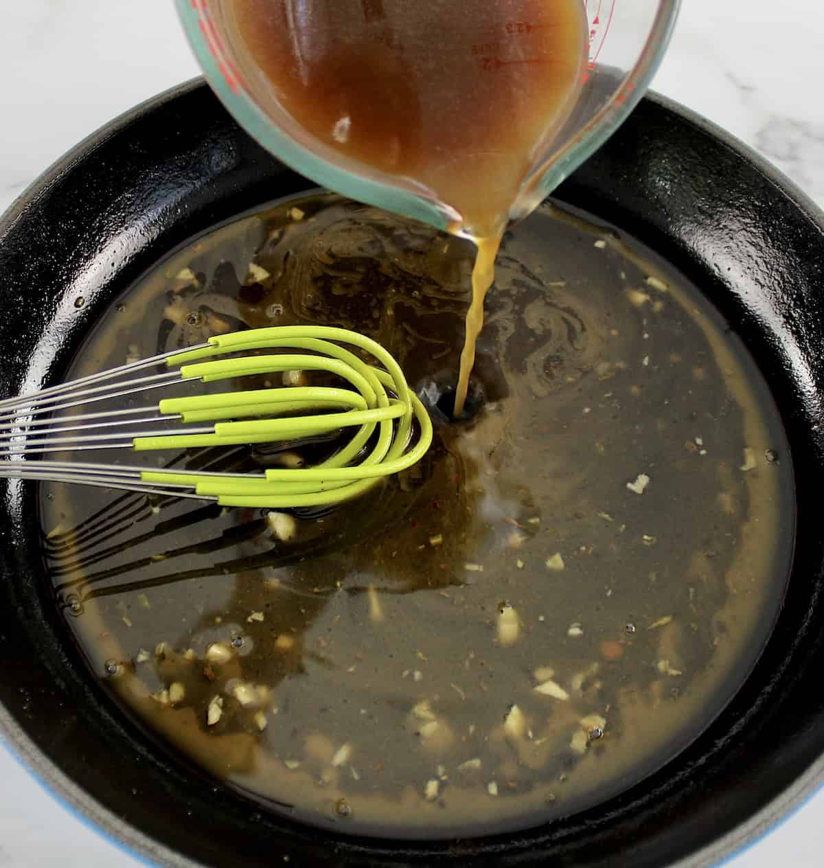 beef broth being poured into skillet with whisk