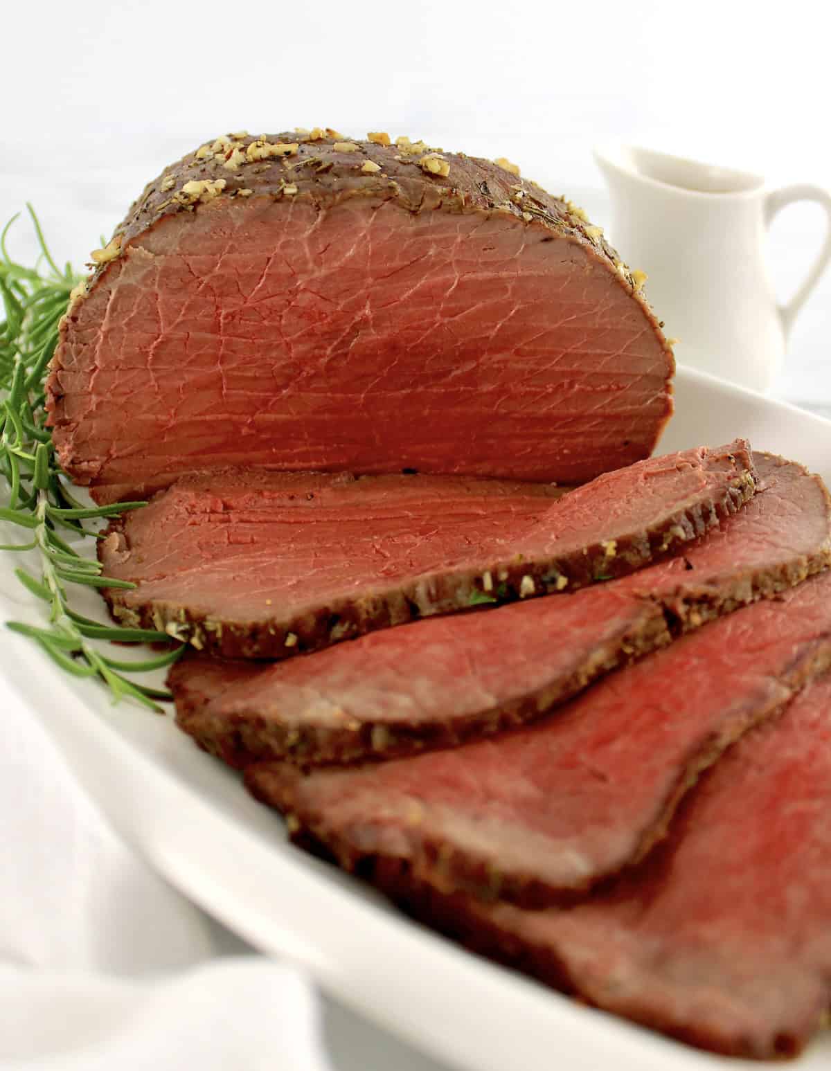 Roast Beef with slices on white platter and rosemary sprig