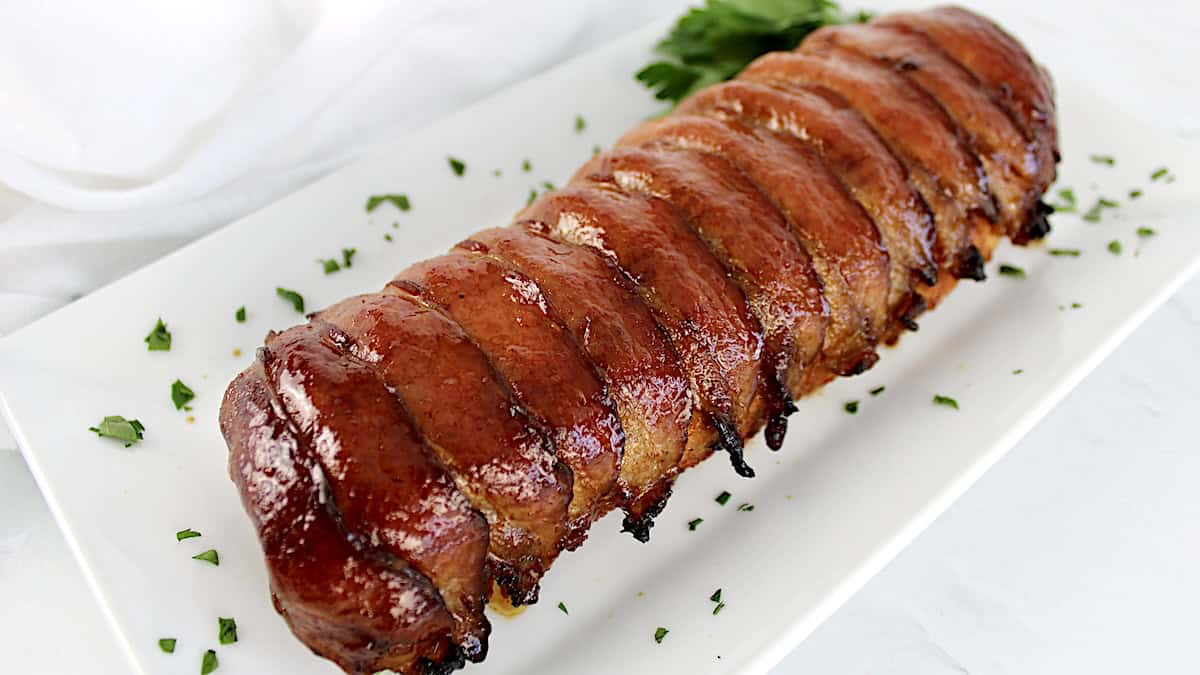 Bacon Wrapped Pork Tenderloin on white plate with parsley