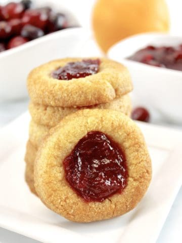 closeup of Cranberry Thumbprint Cookies stacked with one sideways on white plate