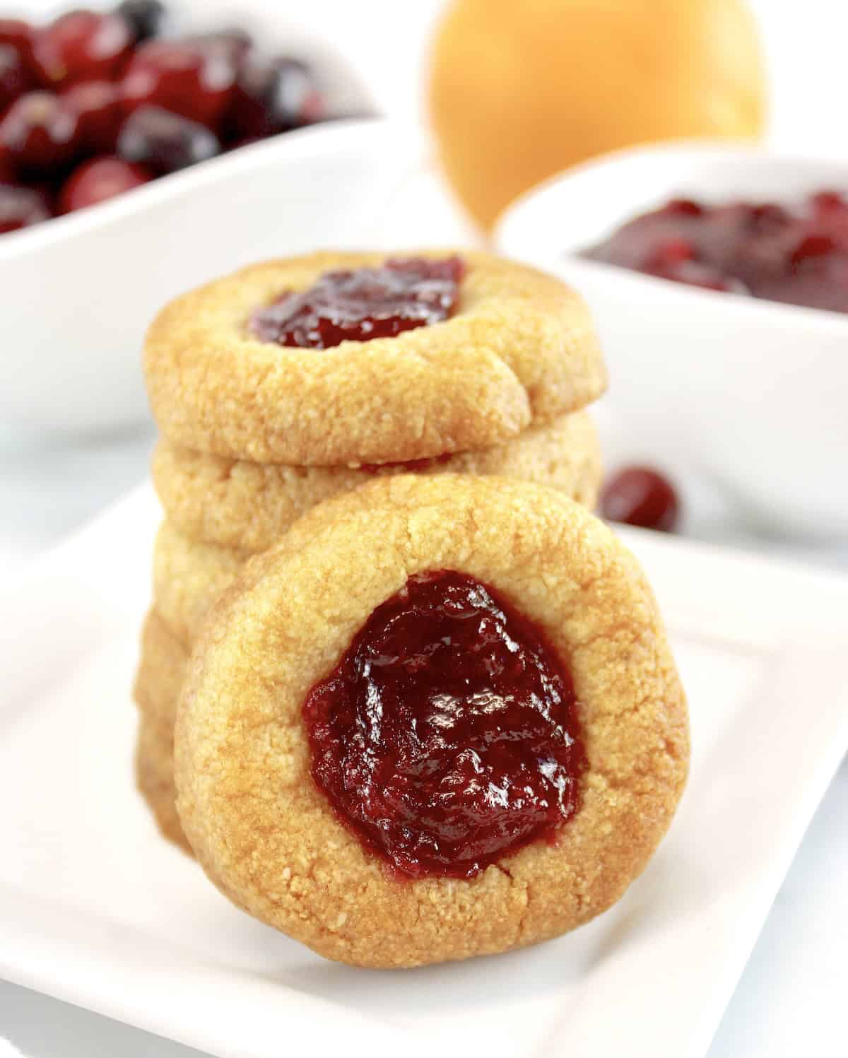 closeup of Cranberry Thumbprint Cookies stacked with one sideways on white plate