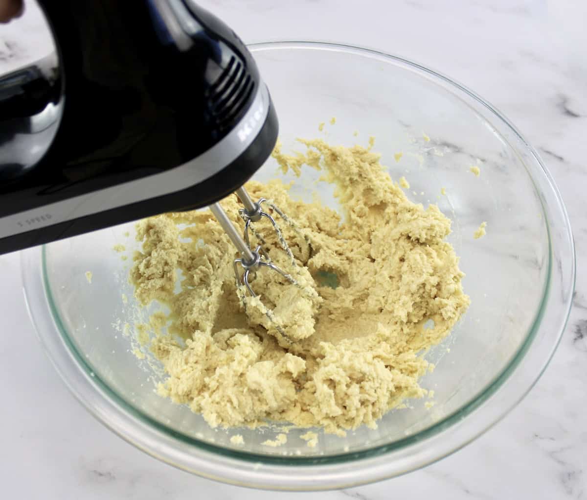 Cranberry Thumbprint Cookie dough in glass bowl being mixed with hand mixer