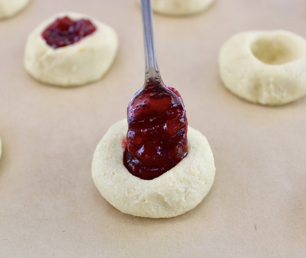 thumbprint cookies being filled with cranberry sauce