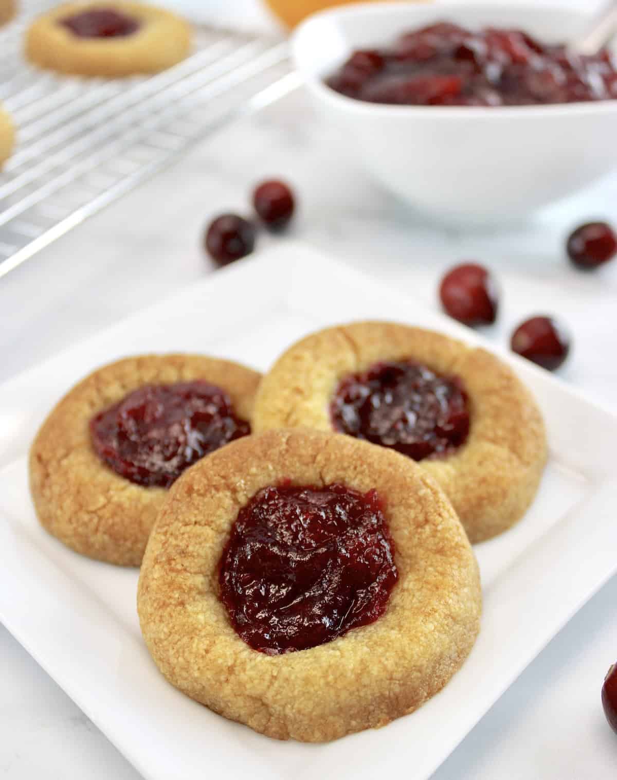 3 Cranberry Thumbprint Cookies on white plate with cranberries in back