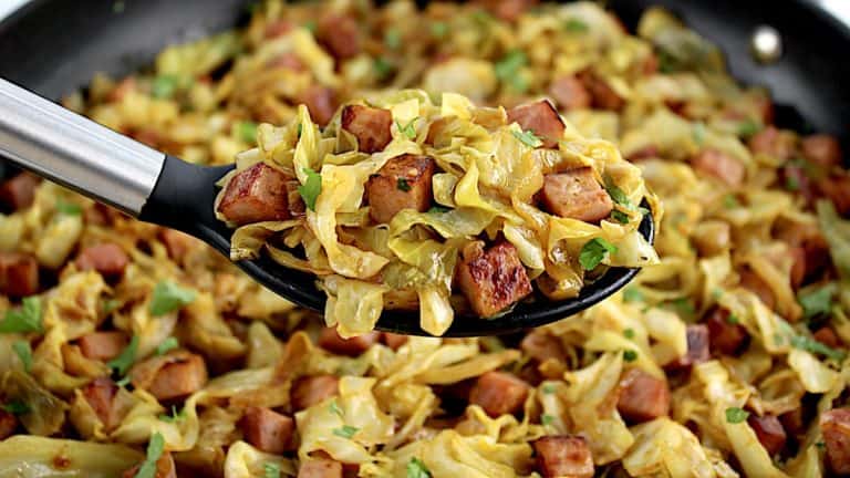 Fried Cabbage with Ham in black serving spoon held up over skillet