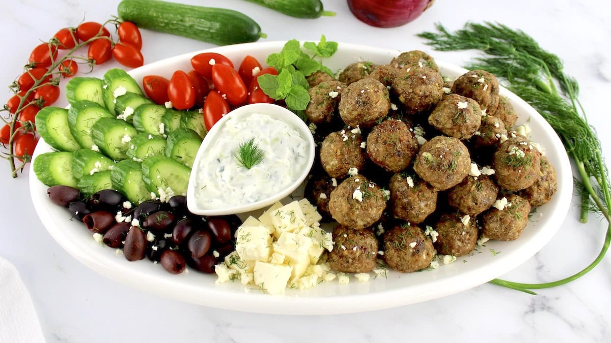 greek meatballs on platter with veggies and dipping sauce in center