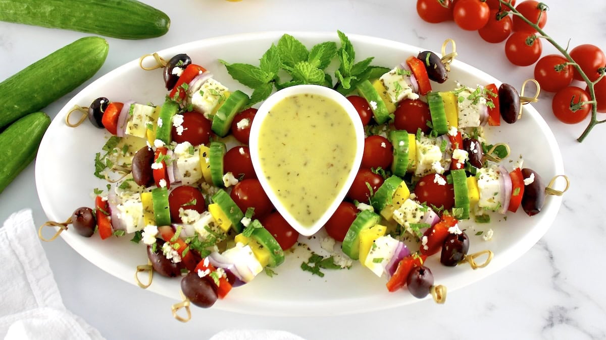 Greek Salad Skewers arranged on white oval platter with dressing in center