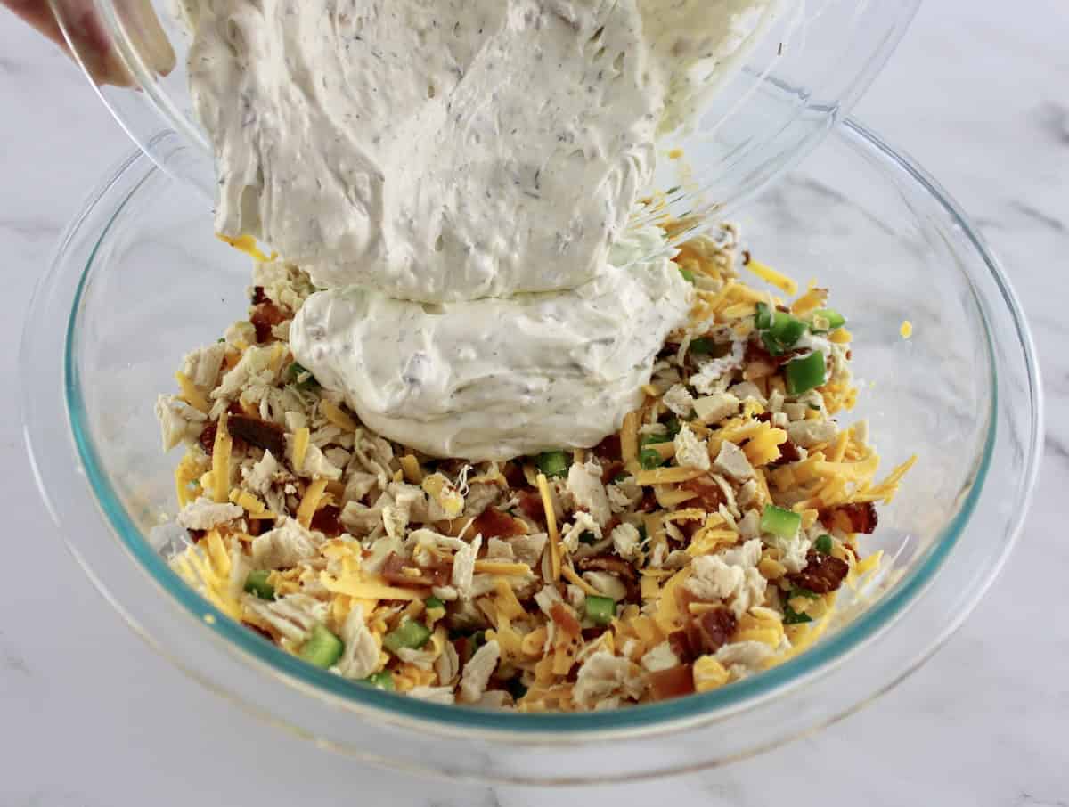 Jalapeño Popper Chicken Dip ingredients in glass bowl with dressing being poured over top