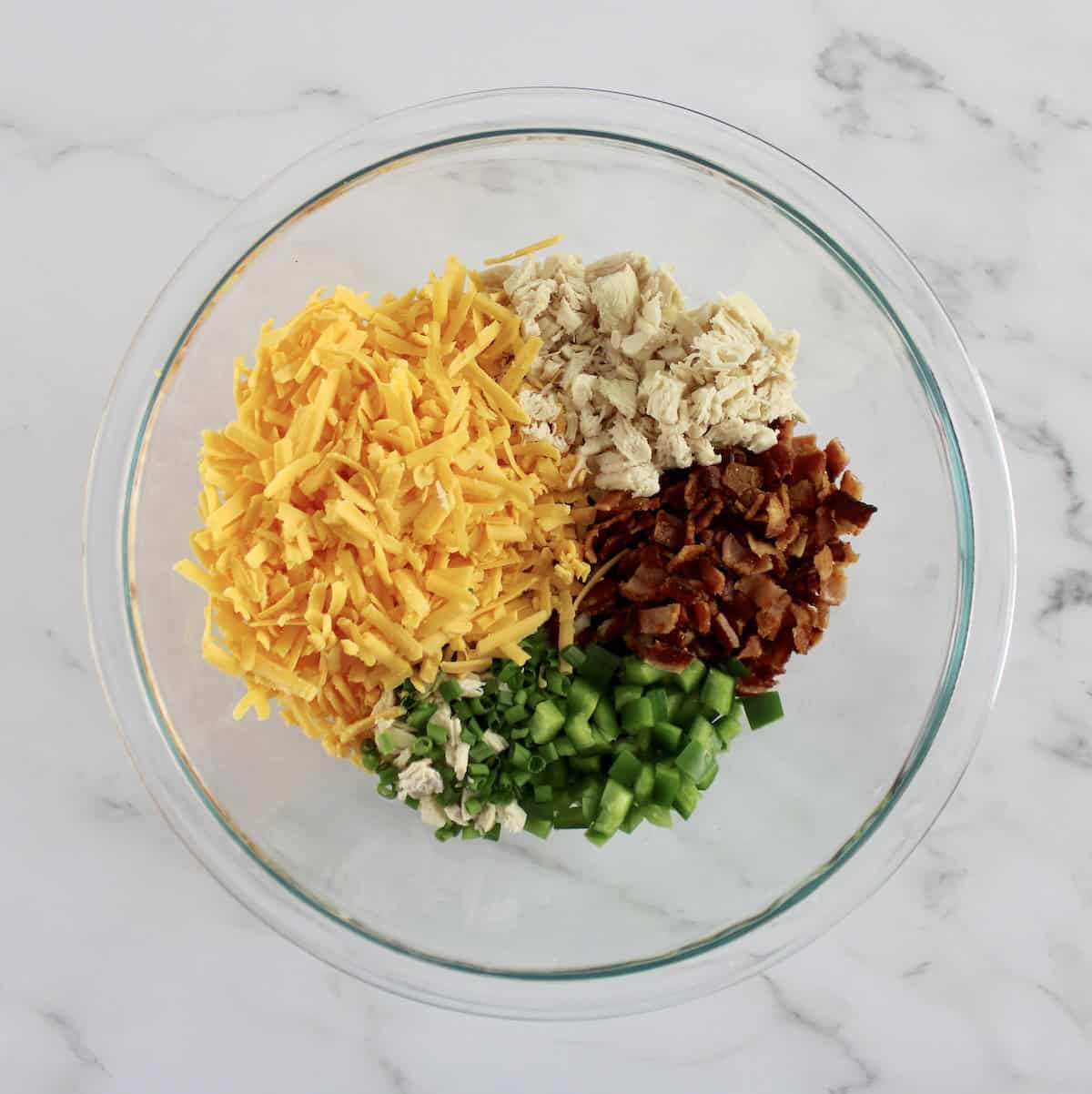 Jalapeño Popper Chicken Dip ingredients in glass bowl in sections