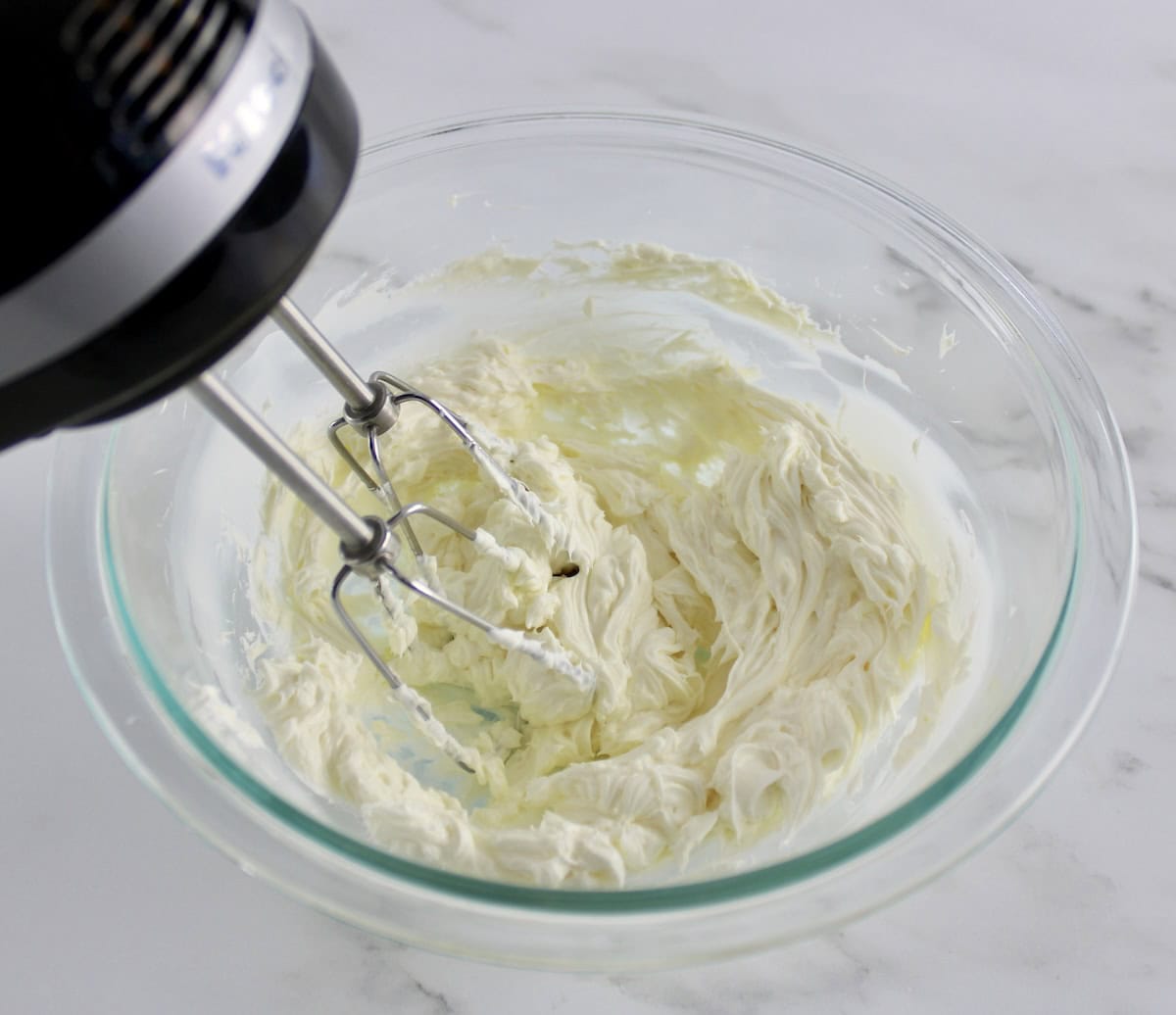 cream cheese being whipped in glass bowl with hand mixer