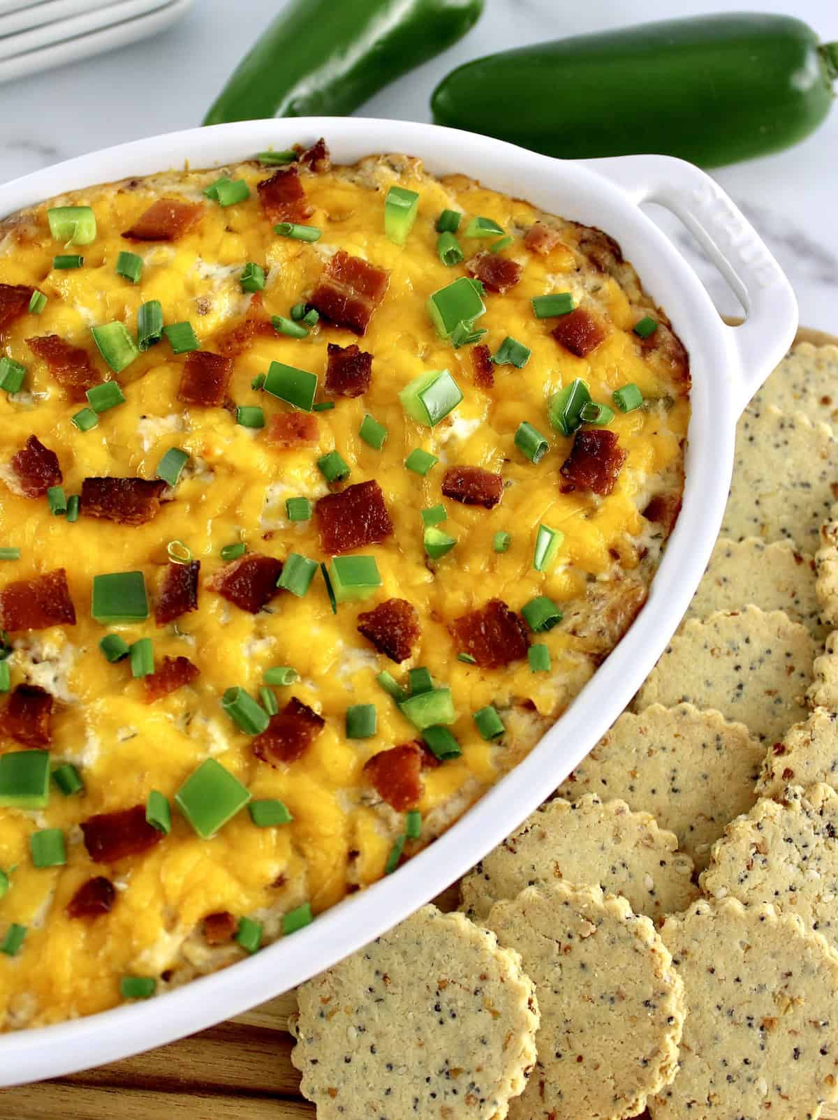 closeup of Jalapeño Popper Chicken Dip in white casserole with crackers on side