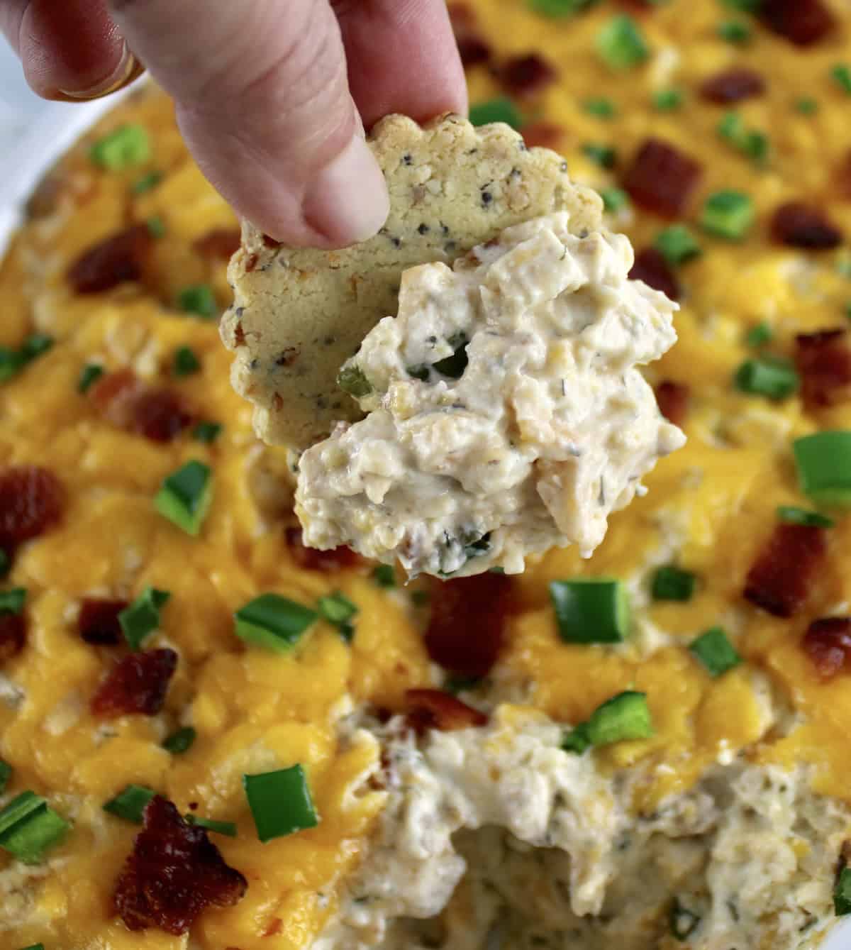 holding up cracker with Jalapeño Popper Chicken Dip on it over casserole