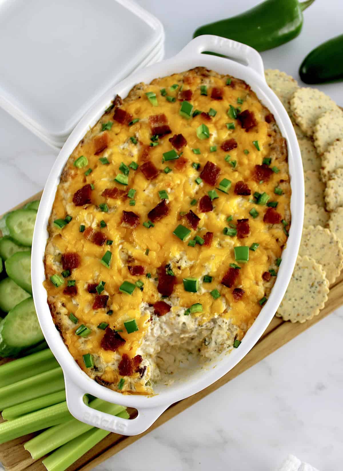 overhead view of Jalapeño Popper Chicken Dip in white casserole with some missing and veggies and crackers on side