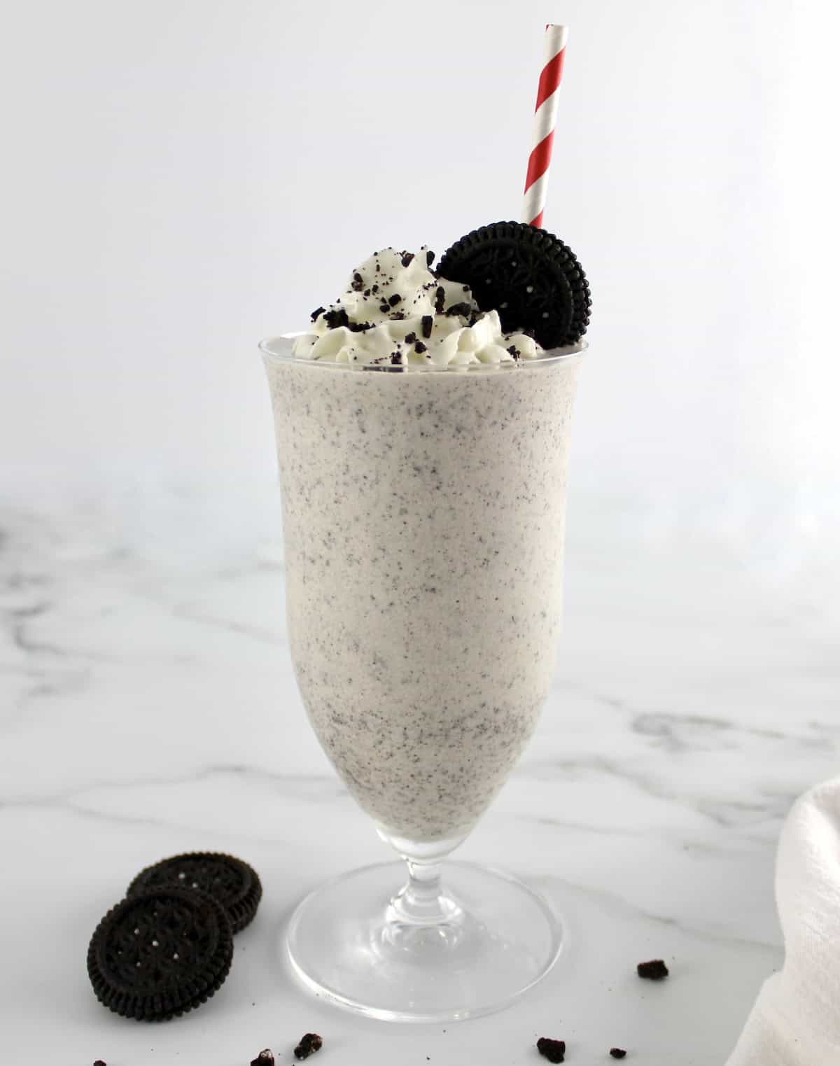 side view of Keto Cookies and Cream Milkshake in glass with cookie on top and red and white straw