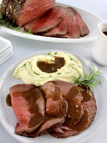 Roast Beef with Gravy on plate with mashed cauliflower and gravy with roast in back