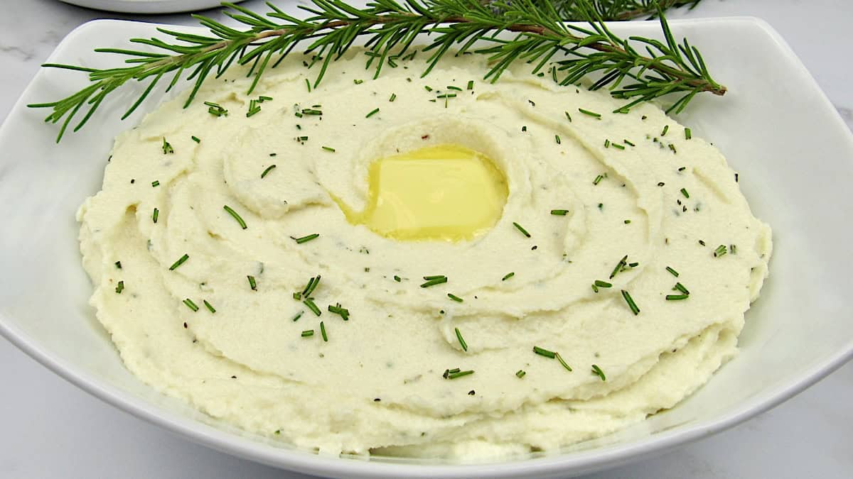 white bowl with mashed cauliflower with rosemary sprig garnish