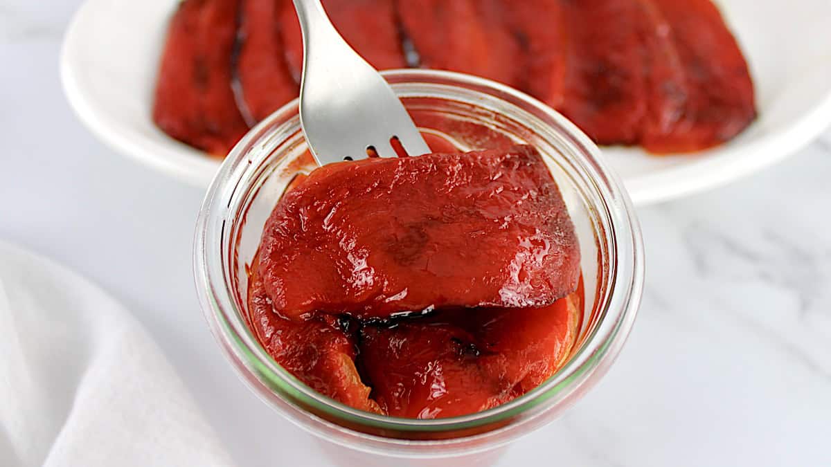 Roasted Red Peppers being lifted with fork out of glass jar