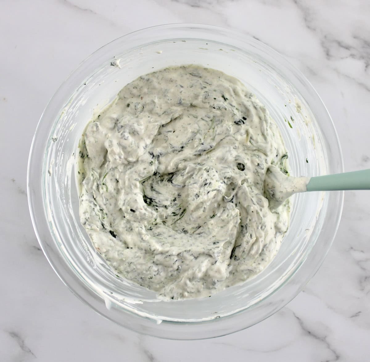 Spinach Dip in glass bowl with blue spoon