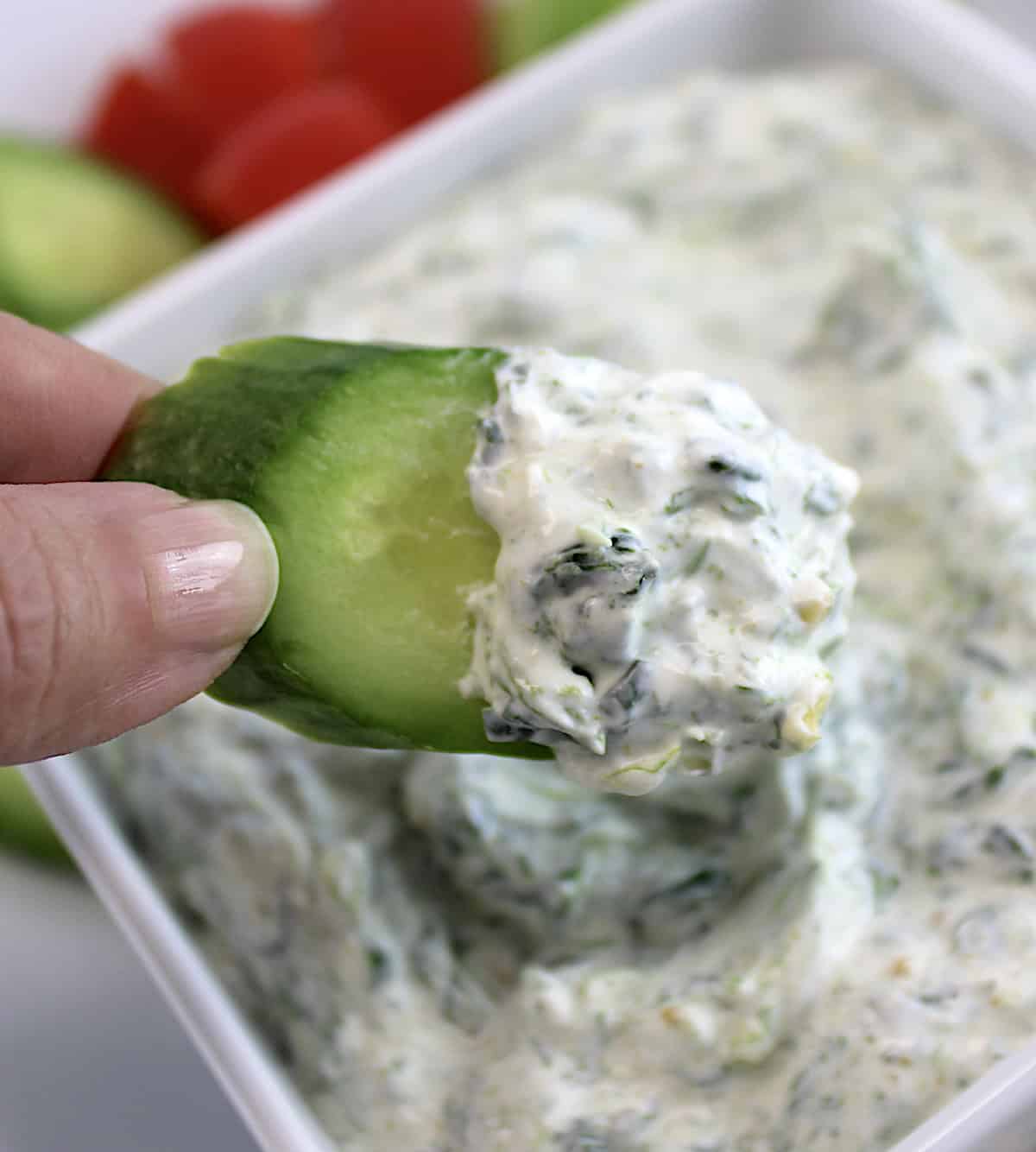 holding up cucumber slice dipped in Spinach Dip