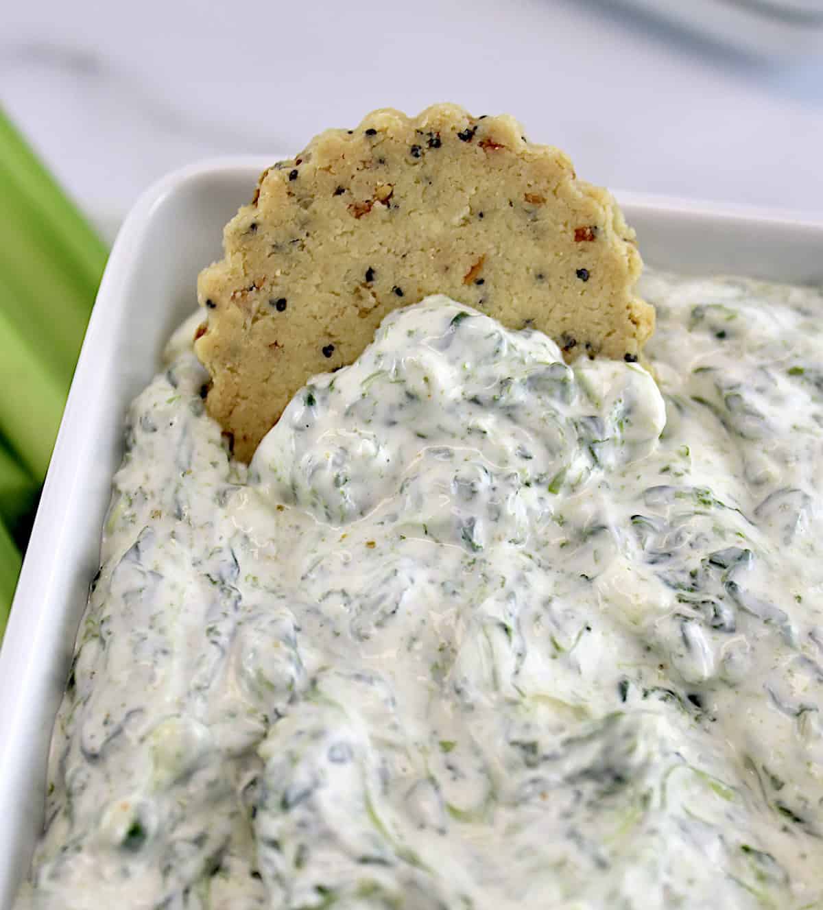 Spinach Dip in white square bowl with cracker sticking up out of it