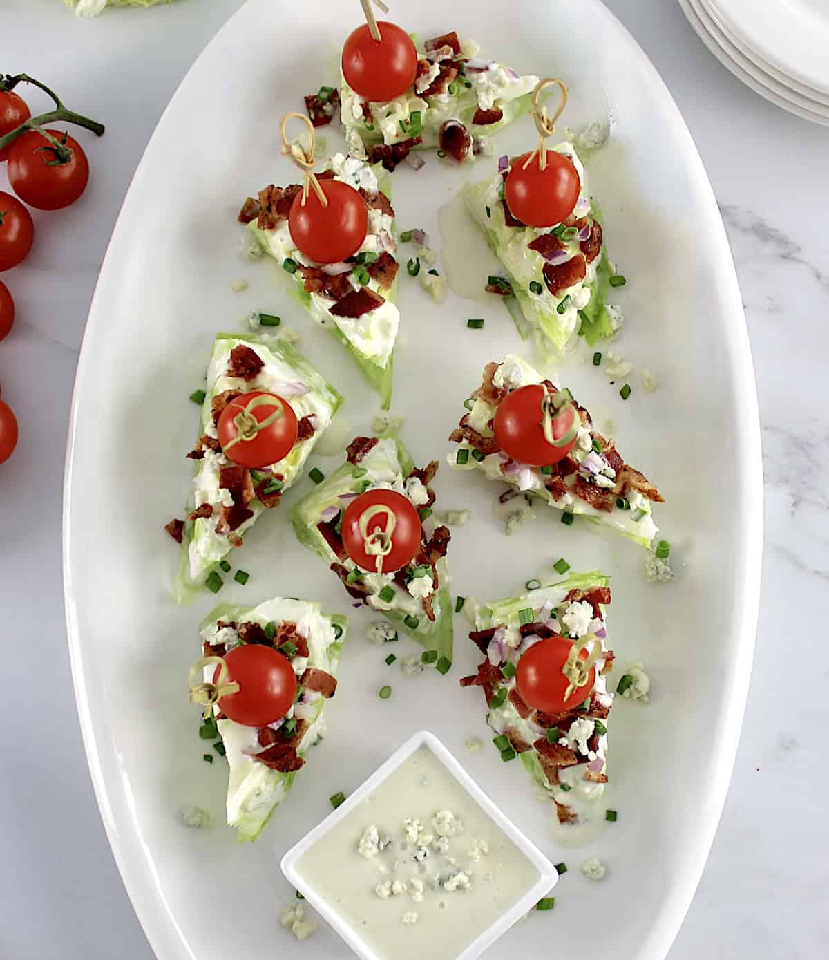 overhead view of Wedge Salad Bites on white plate with cherry tomato through toothpick