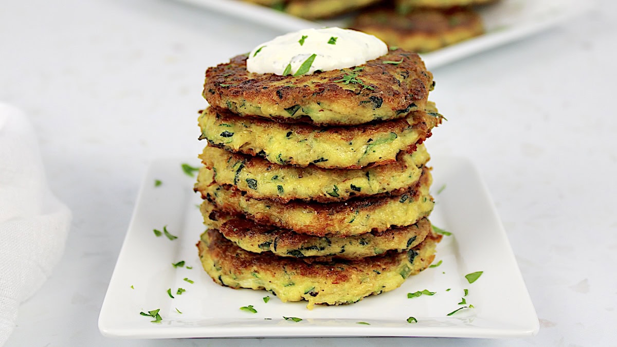 Keto Zucchini Fritters stacked up on white plate with dipping sauce on top