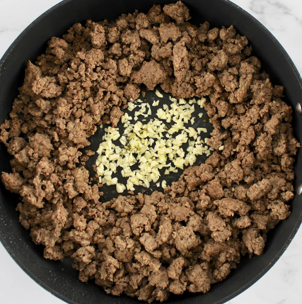 cooked ground beef in skillet with minced garlic in center