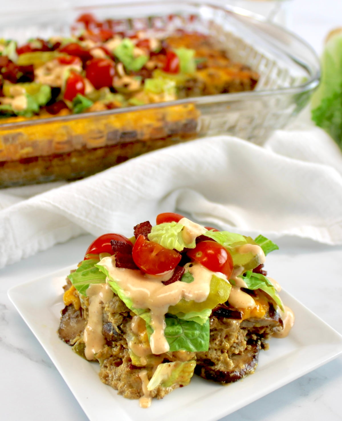 closeup of Bacon Cheeseburger Casserole with lettuce, tomatoes and pickles on top