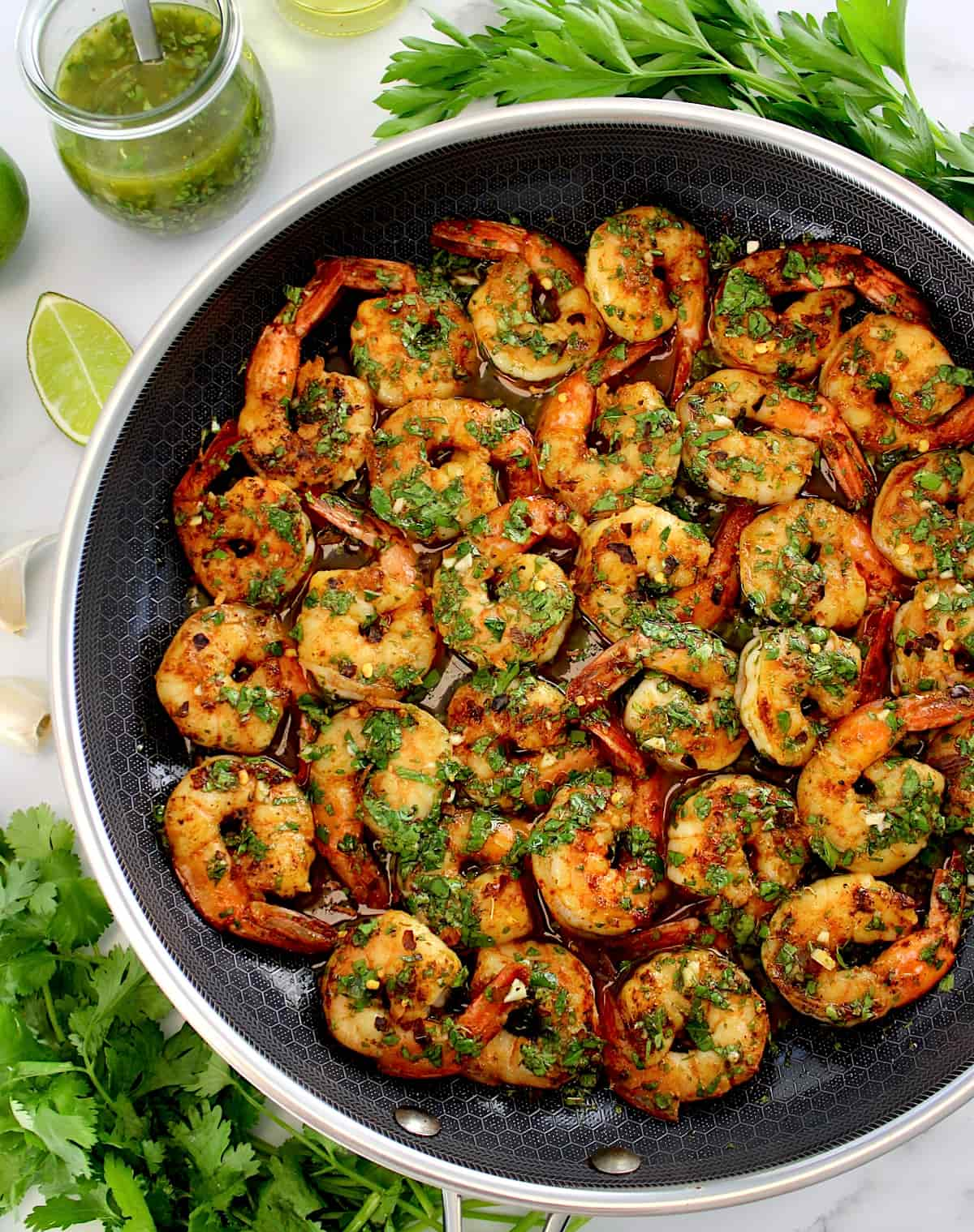 Chimichurri Shrimp in skillet with sauce and fresh herbs in back