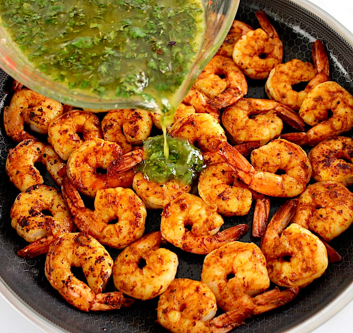 Chimichurri sauce being poured over cooked smoked paprika shrimp in skillet