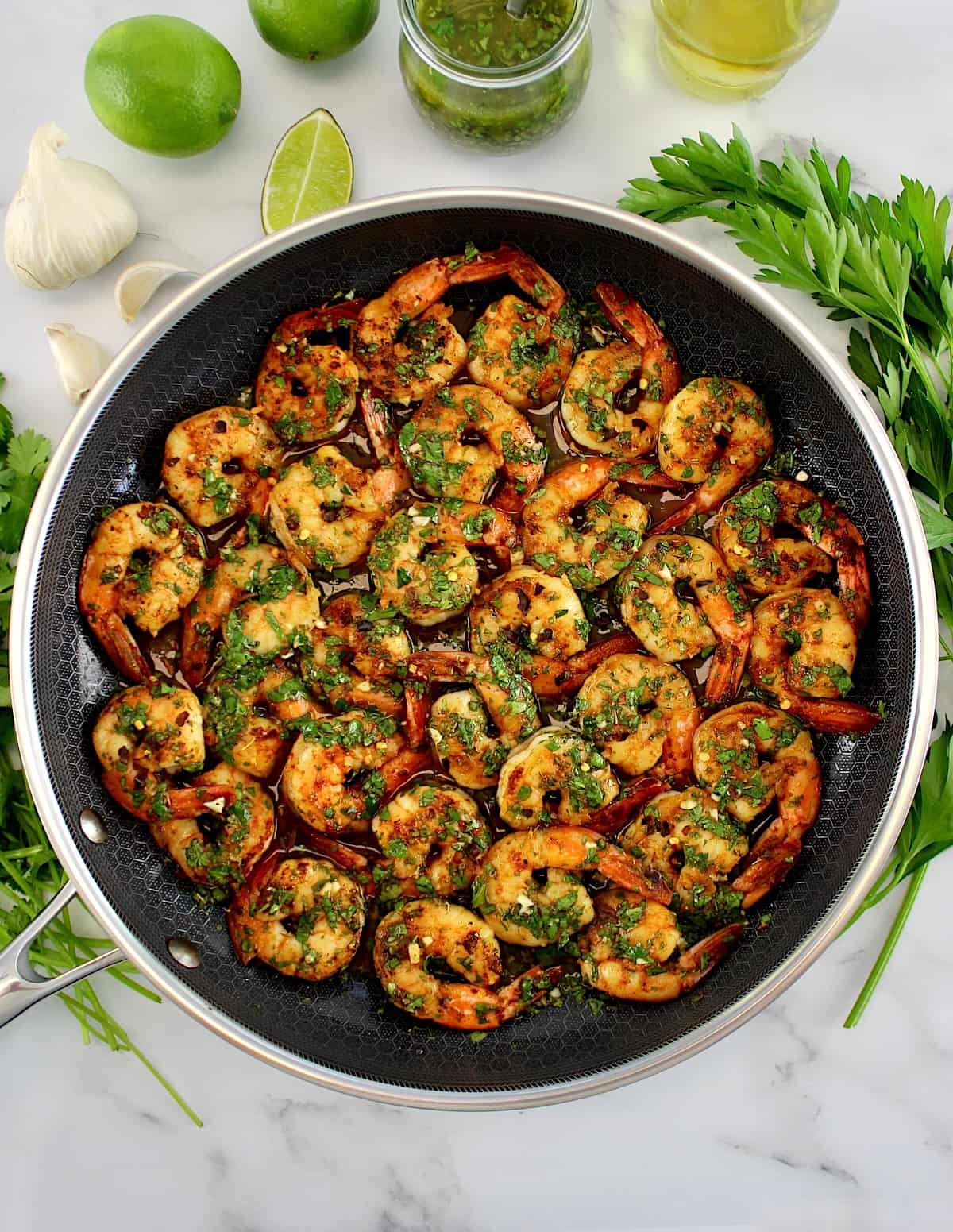 Chimichurri Shrimp in skillet with sauce and fresh herbs in back