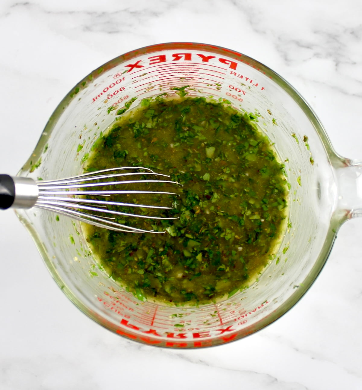 Chimichurri sauce in pyrex measuring cup with whisk