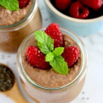 closeup of Chocolate Chia Seed Pudding in open glass jar with raspberries and mint sprig on top