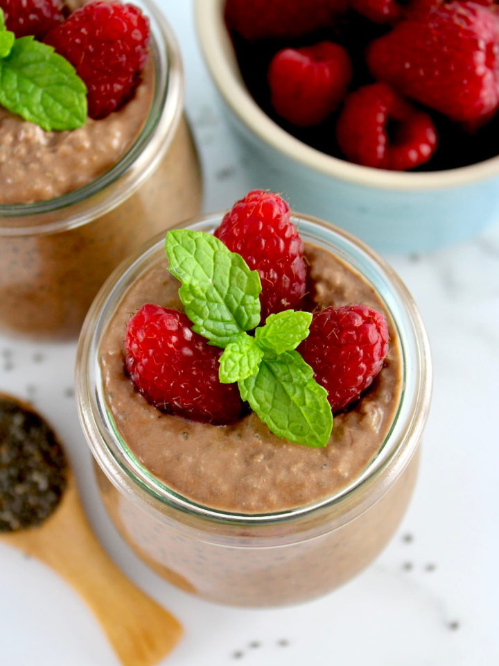 closeup of Chocolate Chia Seed Pudding in open glass jar with raspberries and mint sprig on top