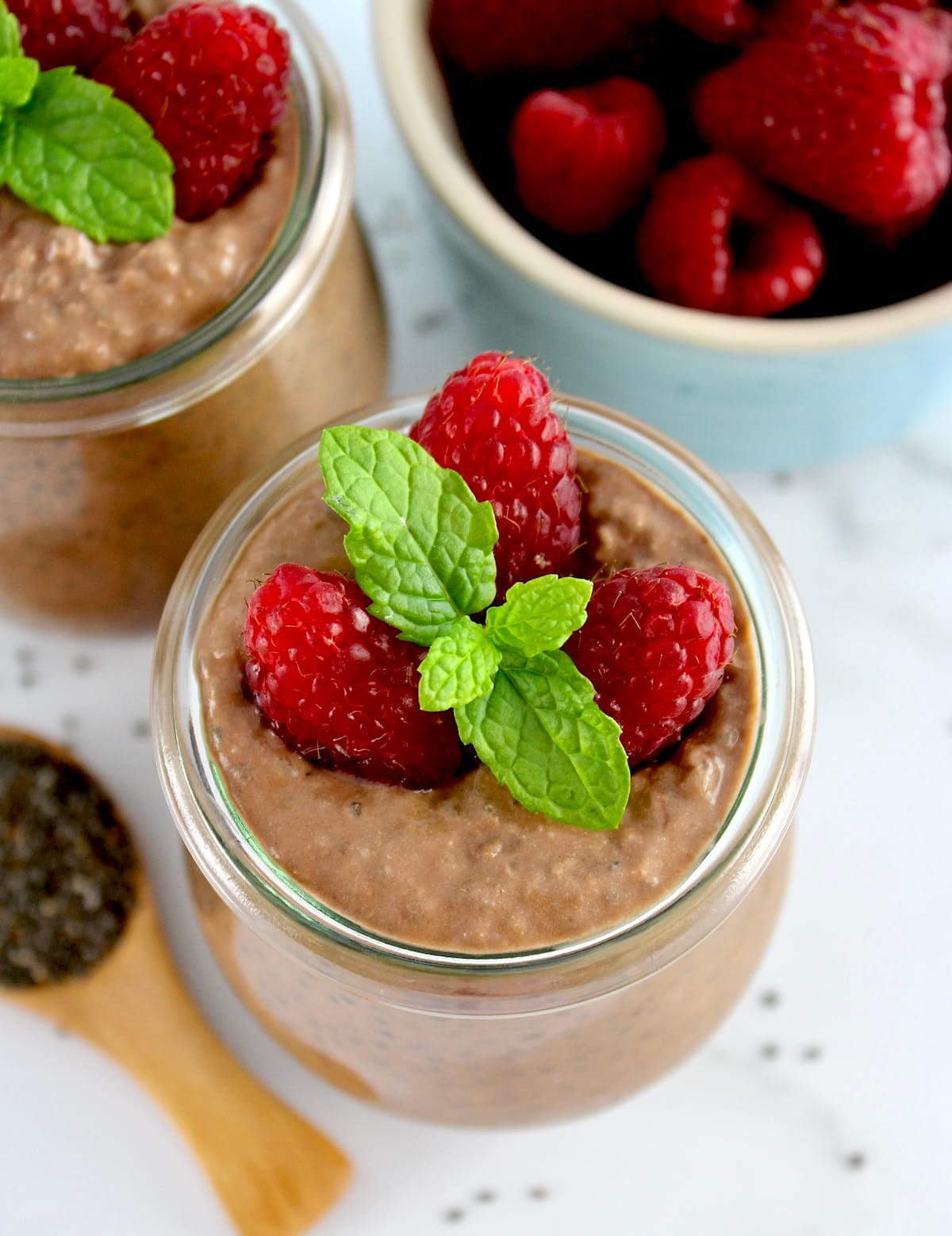 closeup of Chocolate Chia Seed Pudding in open glass jar with raspberries and mint sprig on top