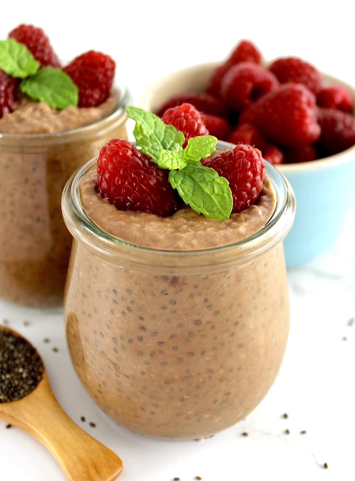 closeup of Chocolate Chia Seed Pudding in open glass jar with raspberries and mint sprig on top