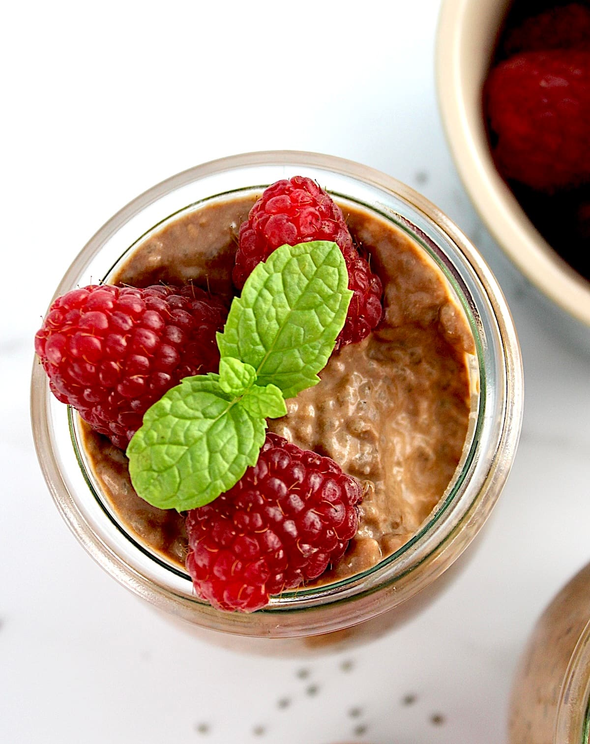 closeup of Chocolate Chia Seed Pudding in open glass jar with raspberries and mint sprig on top