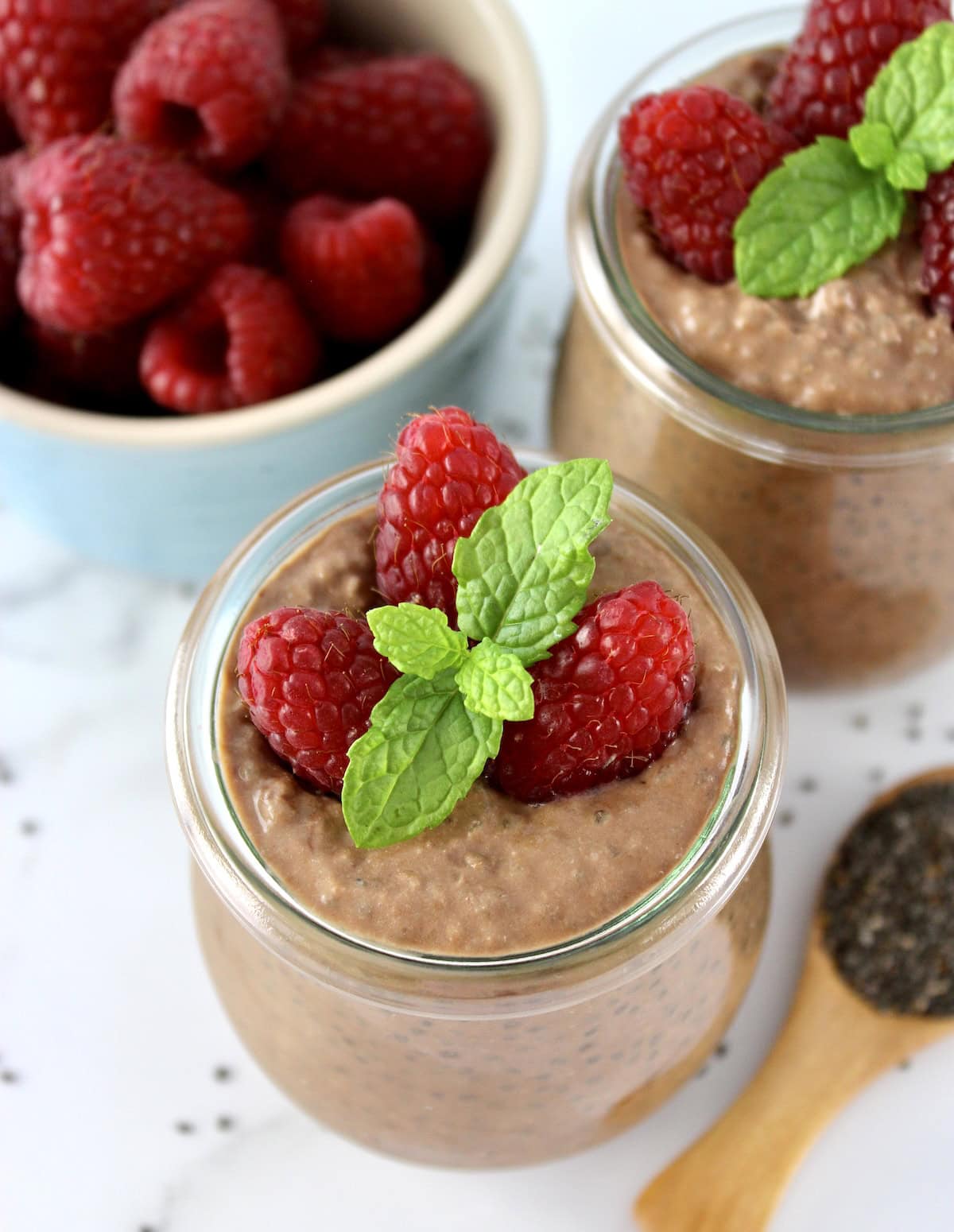 closeup of Chocolate Chia Seed Pudding in open glass jar with raspberries and mint sprig on top