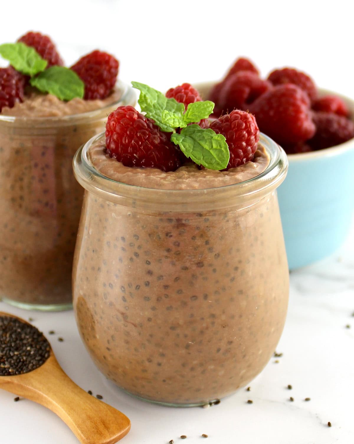 closeup of Chocolate Chia Seed Pudding in open glass jar with raspberries and mint sprig on top