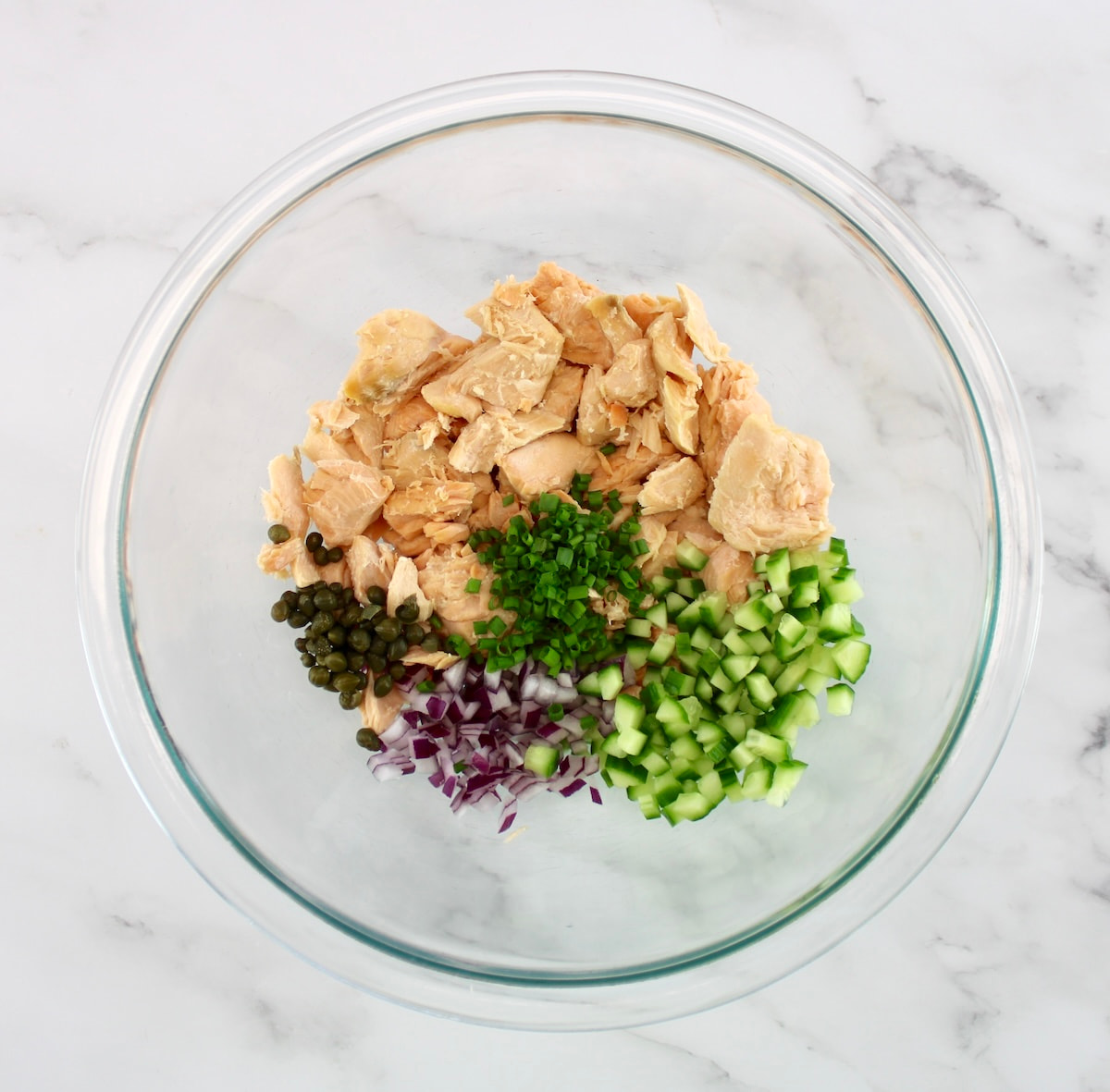 flaked salmon, diced cucumber, red onion, capers and chives in glass bowl unmixed