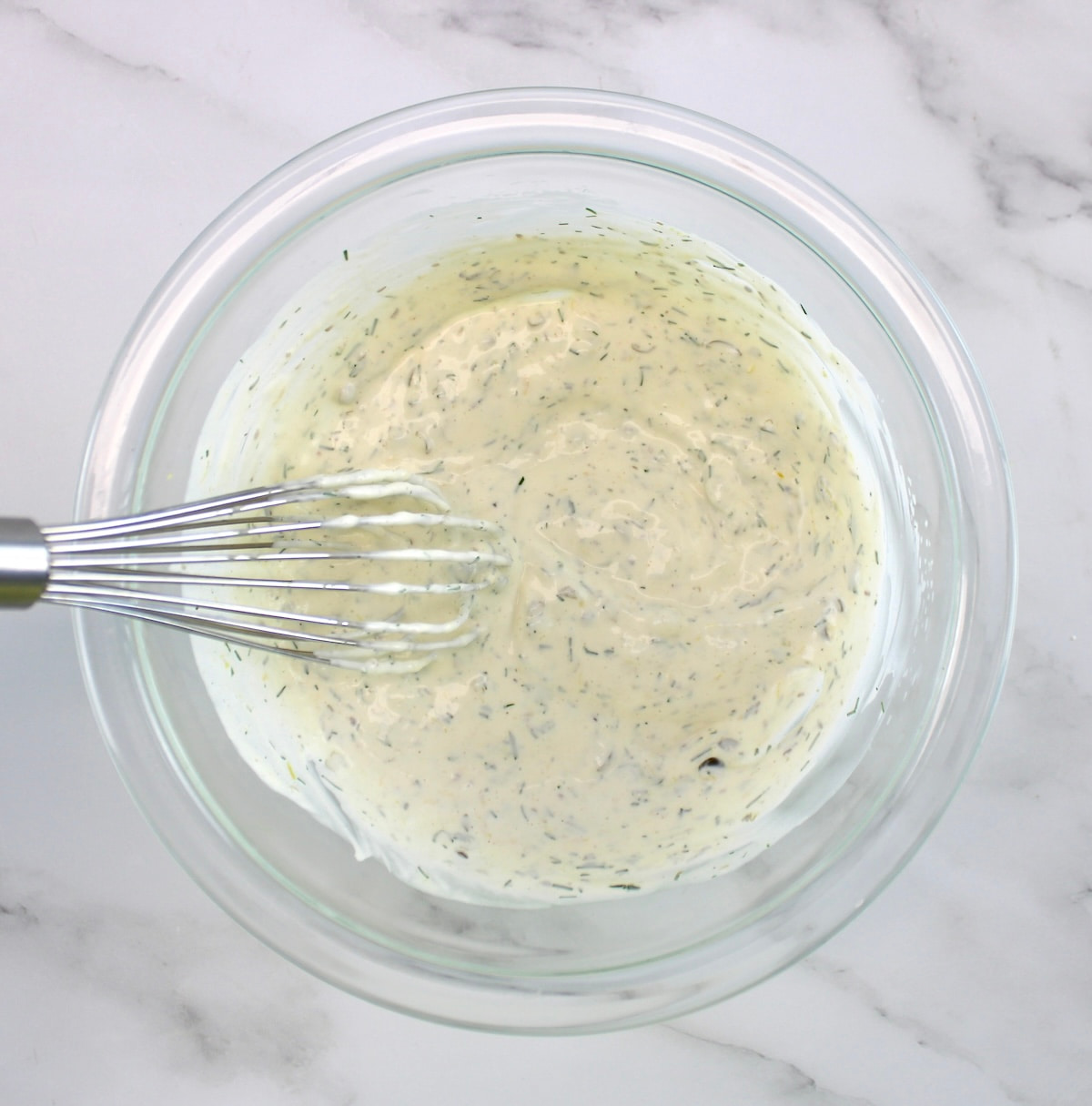 creamy dill sauce in glass bowl with whisk