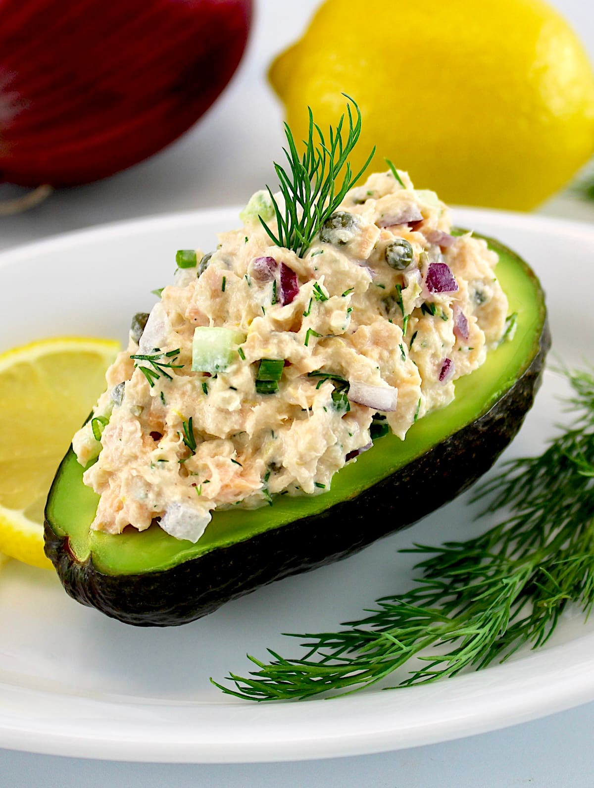 Creamy Dill Salmon Salad in avocado on white plate with lemon slices and fresh dill