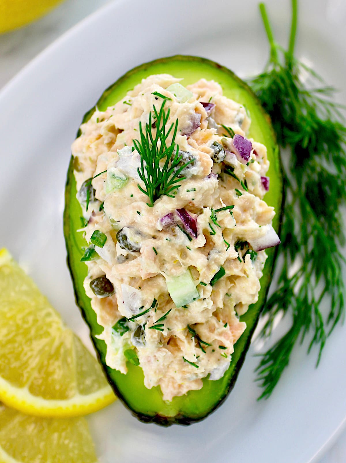 Creamy Dill Salmon Salad in avocado half on white plate with lemon slices and fresh dill