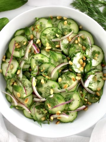 Cucumber Salad in white bowl with cucumber and herbs in back