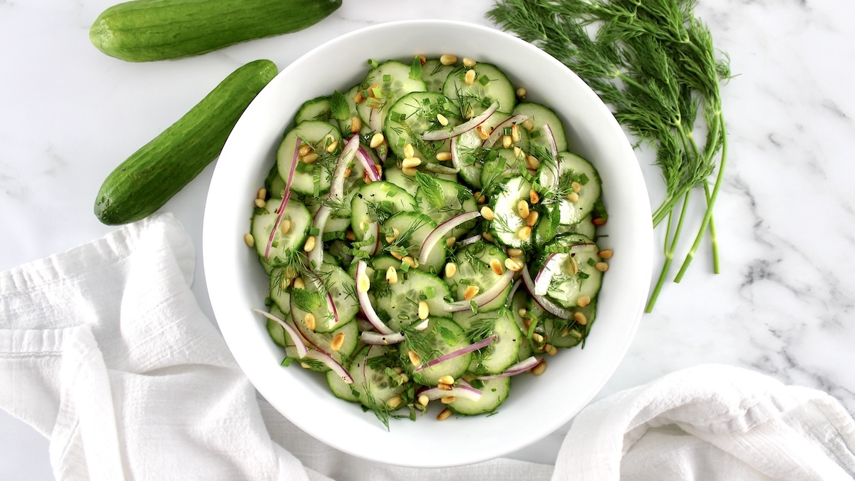 Cucumber Salad in white bowl with cucumber and herbs in back